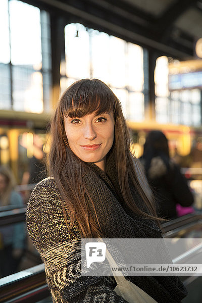 Deutschland  Berlin  Porträt einer lächelnden jungen Frau  die am Bahnsteig wartet