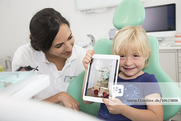 Dentist and smiling girl showing digital tablet in dentist's chair