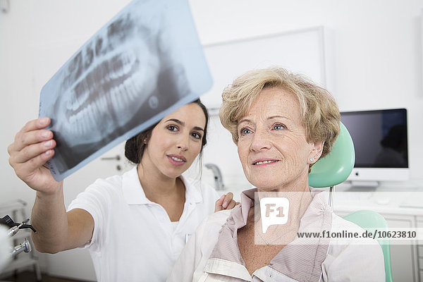 Zahnarzt erklärt Röntgenbild der älteren Frau im Zahnarztstuhl