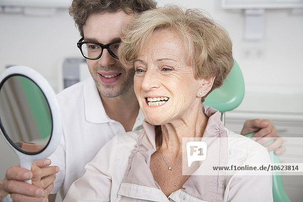 Ältere Frau im Zahnarztstuhl  die ihre Zähne im Spiegel überprüft.