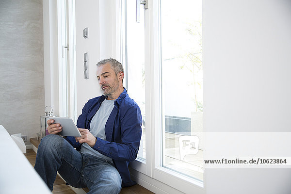 Erwachsener Mann  der von zu Hause aus mit einem digitalen Tablett arbeitet