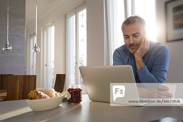Erwachsener Mann  der von zu Hause aus mit dem Laptop arbeitet