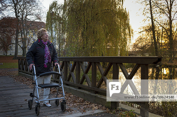 Seniorenfrau mit Rollator  die abends auf einer Fußgängerbrücke läuft.