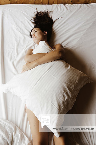 Tagträumende Frau  die auf dem Bett liegt und ihren Körper mit einem Kissen bedeckt.