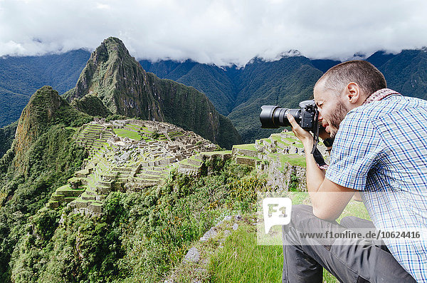 Peru  man taking pictures of Machu Picchu citadel and Huayna Picchu mountain