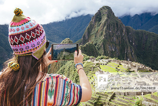Peru  Frau fotografiert die Zitadelle Machu Picchu und den Berg Huayna Picchu mit einer Tafel.
