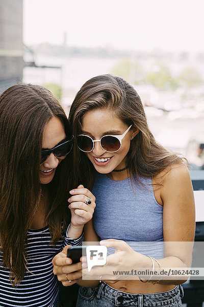 USA  New York City  zwei lächelnde Freunde beim Blick aufs Handy