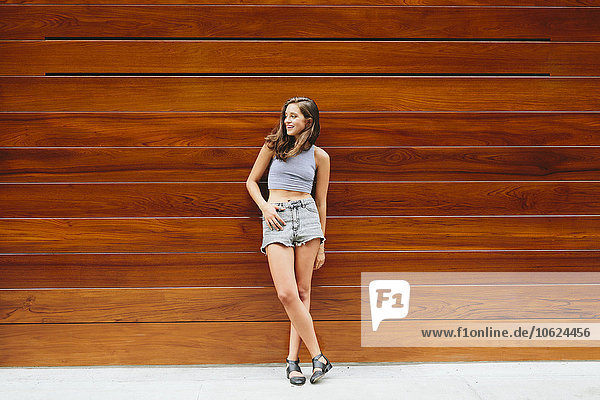 Smiling brunette young woman leaning against wooden wall