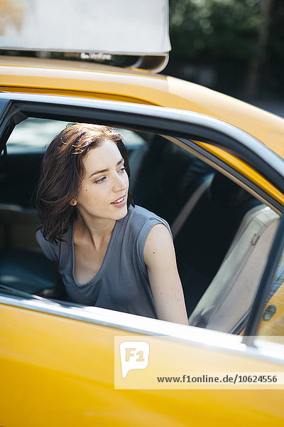 USA  New York City  Porträt einer jungen Frau beim Einsteigen in ein gelbes Taxi