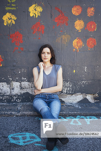 USA  New York City  Porträt einer jungen Frau  die auf dem Boden sitzt und sich an eine Wand lehnt.