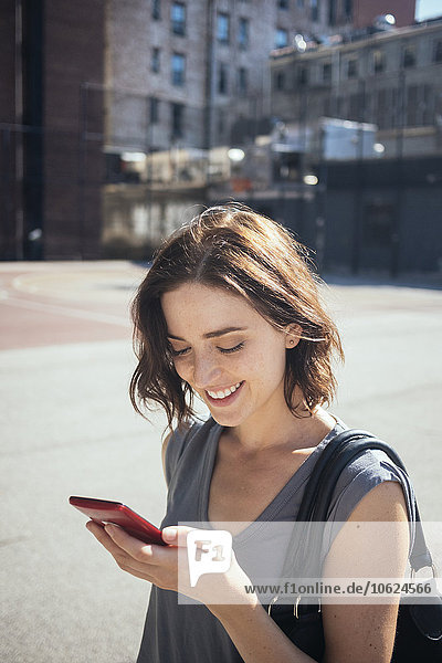 USA  New York City  Manhattan  lächelnde junge Frau beim Blick auf ihr Smartphone