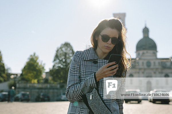 Italien  Vicenza  Frau mit kariertem Mantel und Sonnenbrille beim Blick aufs Handy