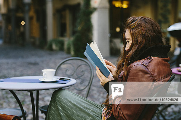 Frau liest ein Buch im Freien in einer kleinen Bar.