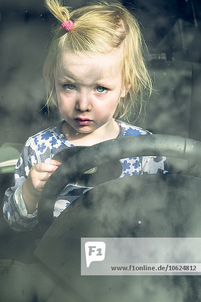 Portrait eines blonden Kleinkindes  das im Auto hinter dem Lenkrad sitzt.
