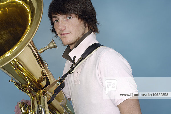 Porträt des Teenagers mit Tuba vor blauem Hintergrund