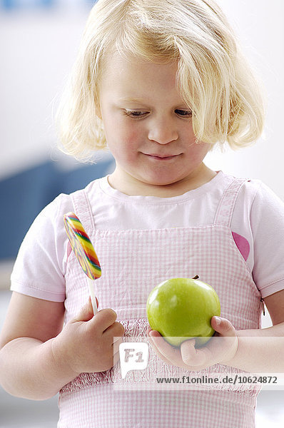 Porträt eines kleinen blonden Mädchens mit einem grünen Apfel und einem Lolli