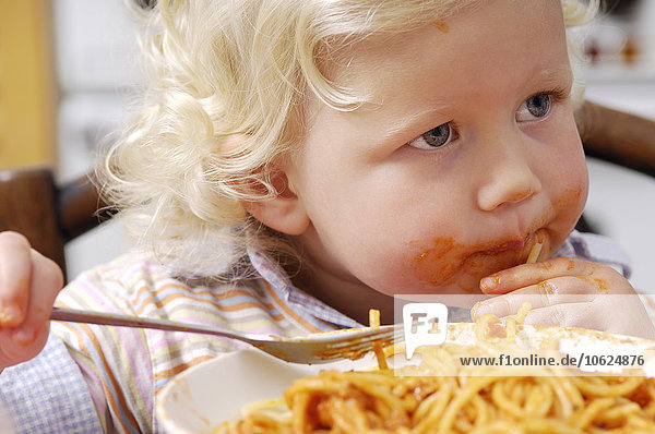 Porträt eines kleinen blonden Mädchens  das Spaghetti mit Tomatensauce isst.