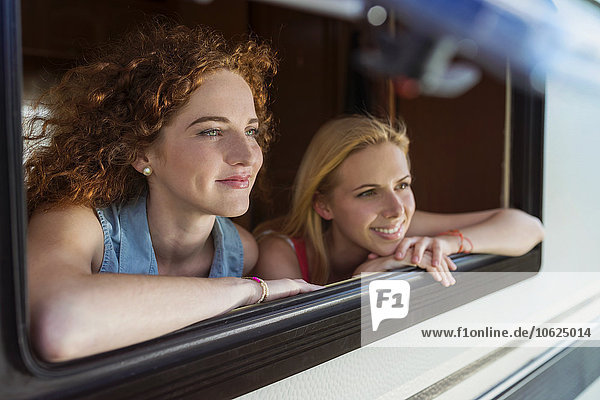 Zwei Freundinnen  die durch das Fenster des Wohnwagens schauen und etwas sehen.