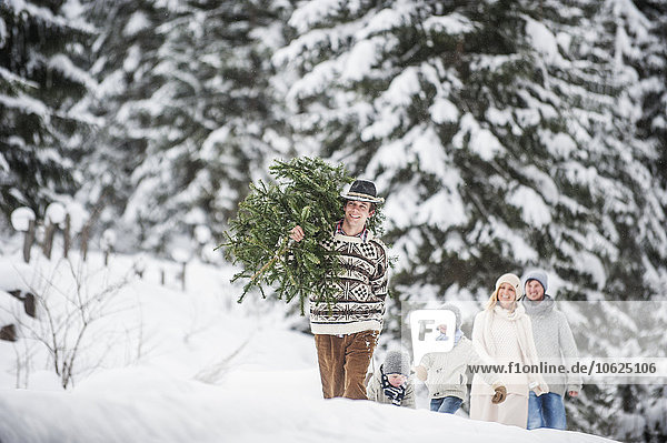 Österreich  Altenmarkt-Zauchensee  Mann mit Weihnachtsbaum und Familie zusammen im Winterwald