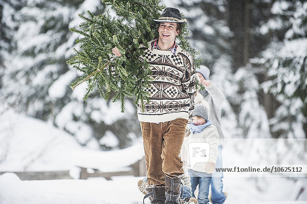 Österreich  Altenmarkt-Zauchensee  glücklicher Mann mit Weihnachtsbaum auf der Schulter im Winterwald