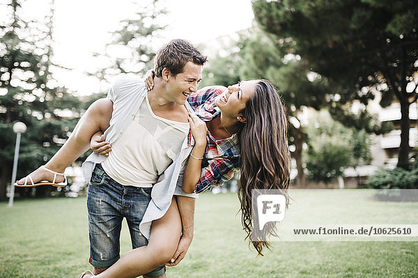 Young man giving his girlfriend a piggy back on a meadow in a park
