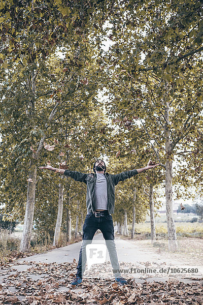 Spain  Tarragona  young man standing on country road throwing autumn leaves in the air