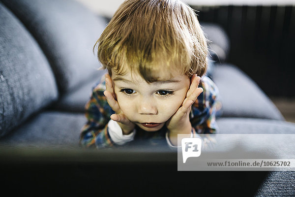 Portrait of little boy lying on the couch looking at digital tablet