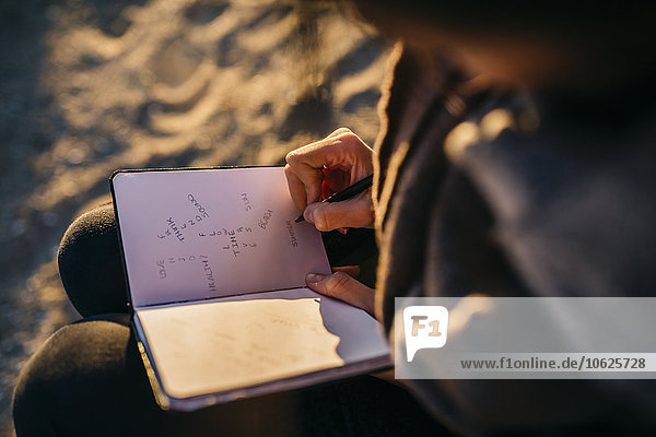 Junge Frau am Strand sitzend mit Notizbuch  Nahaufnahme
