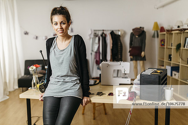 Junge Modedesignerin in ihrem Atelier  an den Schreibtisch gelehnt