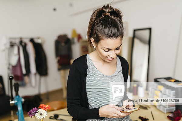 Young fashion designer working in her studio  using smartphone