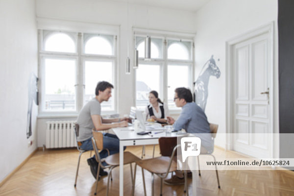Verschwommener Blick auf drei kreative Geschäftsleute bei einem Meeting in einem modernen Büro