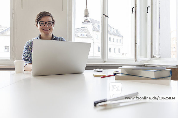 Smiling young businesssman using laptop in a modern office