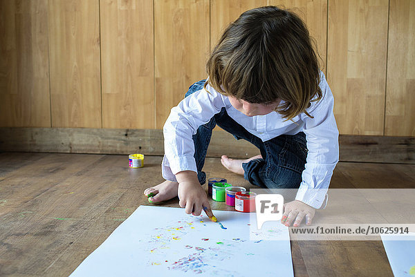 Kleiner Junge kauernd auf Holzbodenmalerei mit Fingerfarben