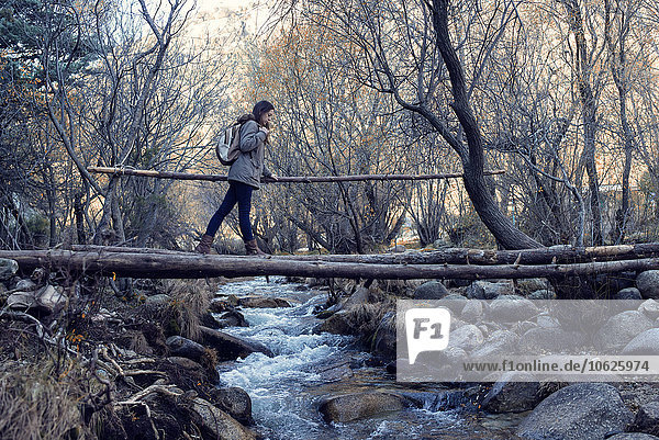 Junge Frau überquert eine Brücke aus Baumstämmen