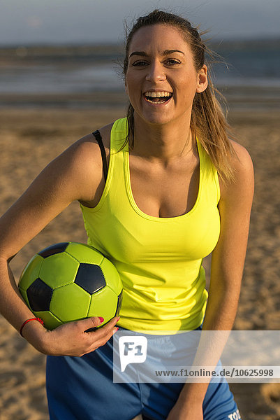 Spanien  Junge Frau beim Fußball spielen am Strand  lachend