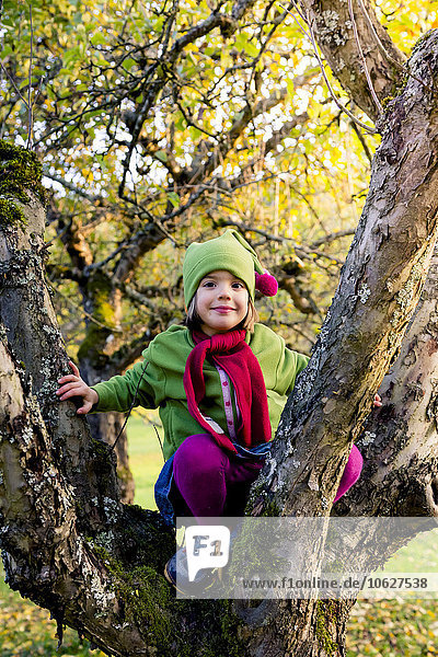 Portrait of smiling little girl sitting on tree trunk