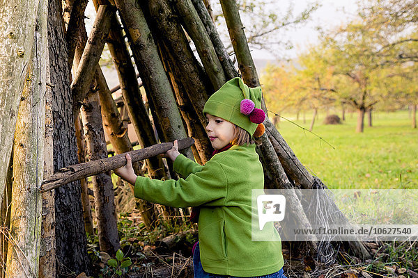 Little girl building a hut with logs on a meadow in autumn