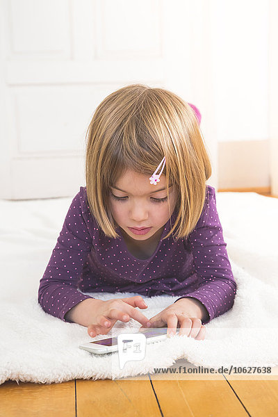 Kleines Mädchen auf der Decke auf dem Boden liegend mit Smartphone