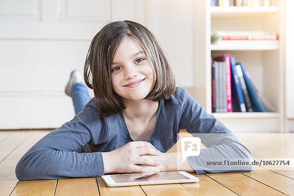 Portrait of smiling girl lying on wooden floor with digital tablet