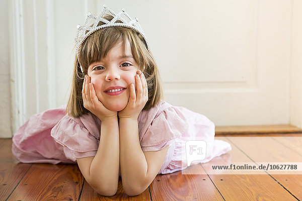 Porträt eines lächelnden kleinen Mädchens  verkleidet als Prinzessin auf dem Holzboden.