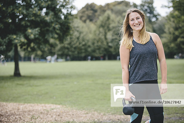 Lächelnde junge Frau mit Kesselglocke im Park