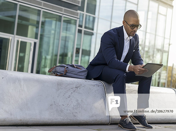 Germany  Cologne  Young businessman sitting on bench  using digital tablet