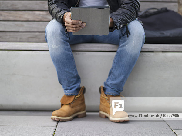 Deutschland  Köln  Junger Mann auf Bank sitzend mit digitalem Tablett
