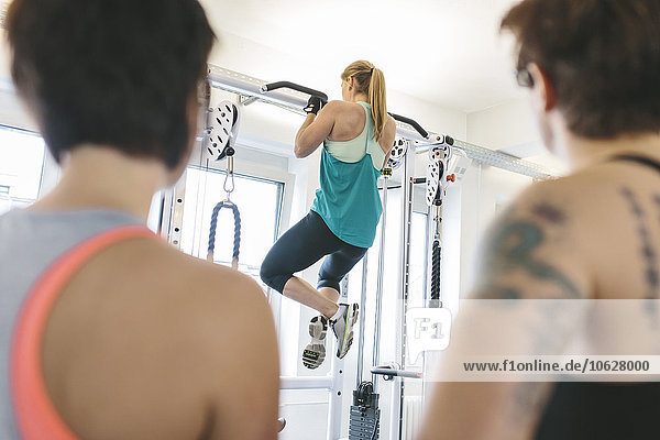 Two women watching athlete doing pull-ups in gym