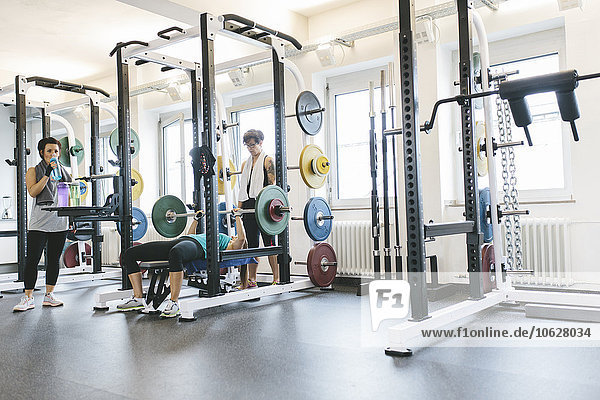 Three women doing barbell bench presses in a power rack