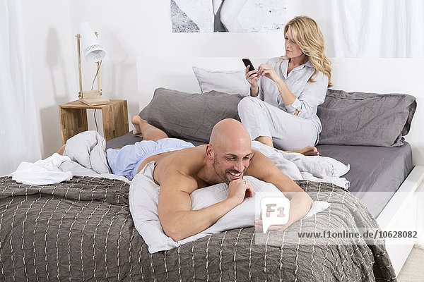 Mature couple in bedroom using their mobile phones