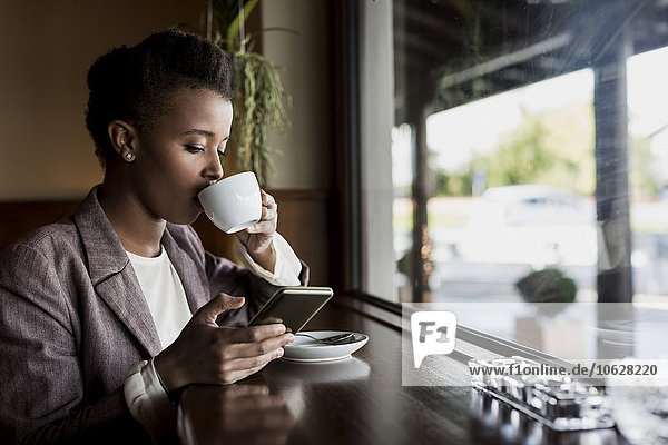 Junge Frau sitzt in einem Café und trinkt Kaffee mit dem Smartphone.