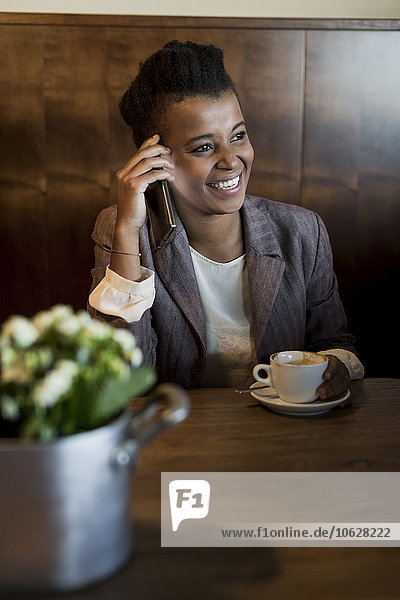 Porträt einer lächelnden jungen Frau  die in einem Café sitzt und mit einem Smartphone telefoniert.