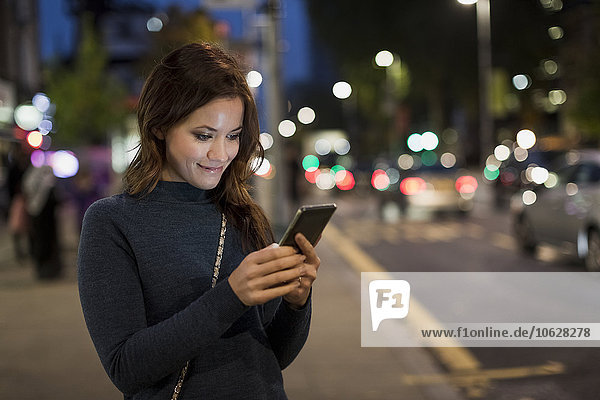 Frau überprüft ihr Smartphone am Straßenrand