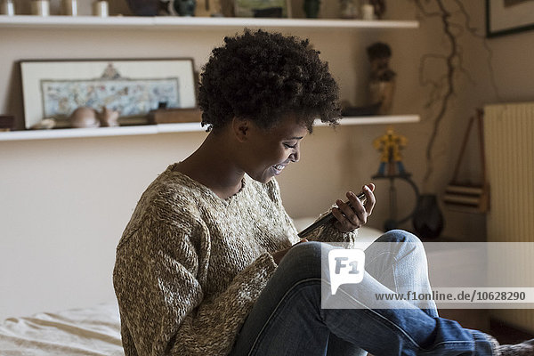 Smiling young woman at home looking at smartphone